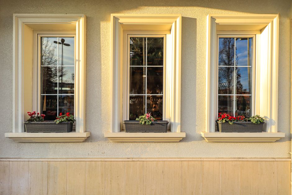 Elegant building facade featuring three windows with vibrant flowerpots on the sills at sunset.